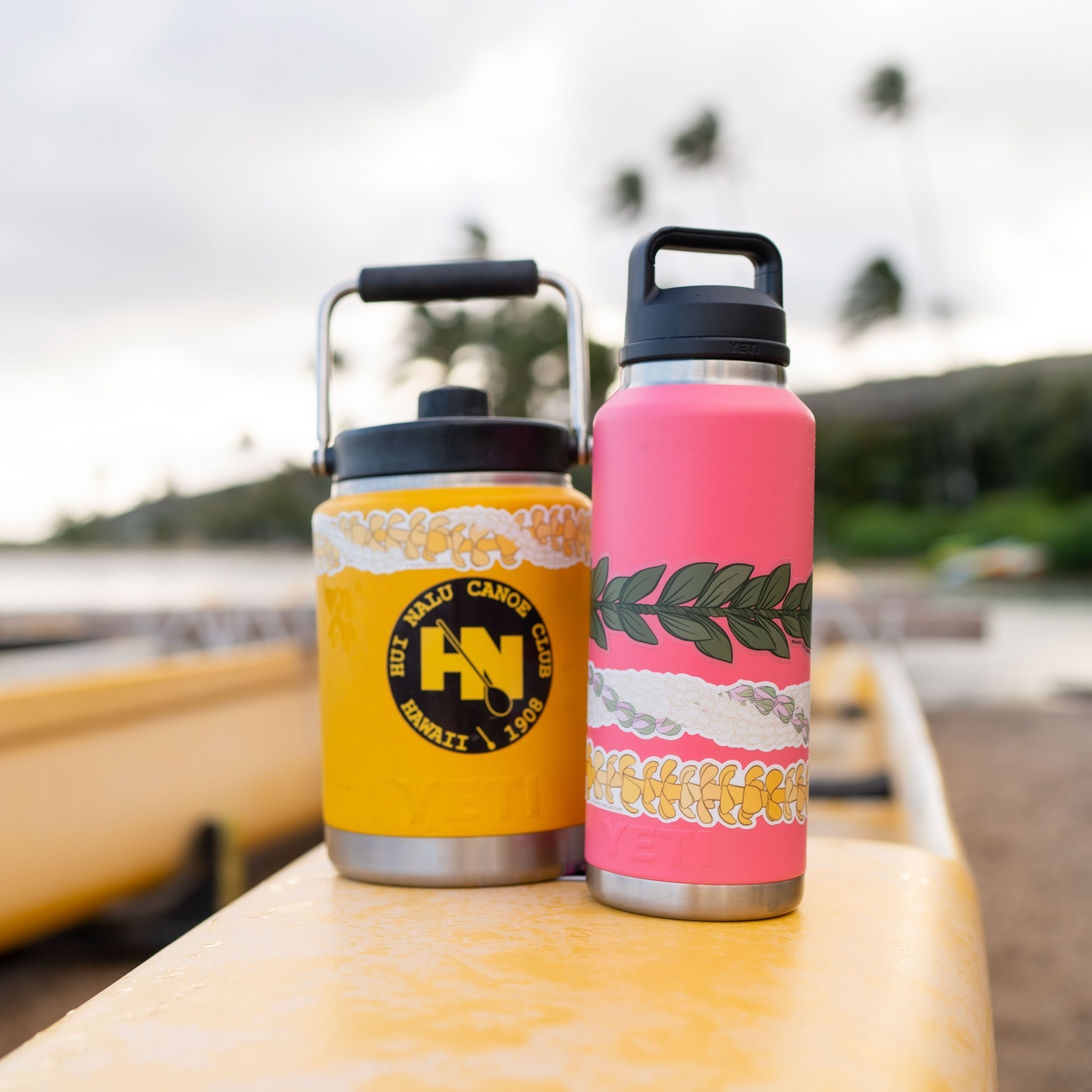 Two insulated stainless steel water bottles on a yellow dock outdoors showcasing stickers