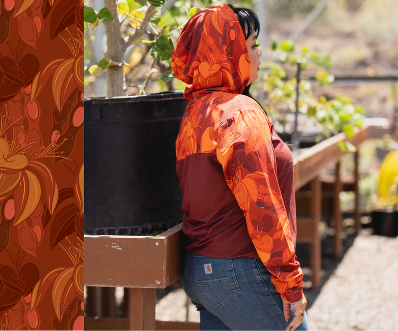 Person wearing a red and orange patterned hoodie in a garden setting, with 'Käköu Collective Dry Forest Collection WILIWILI'